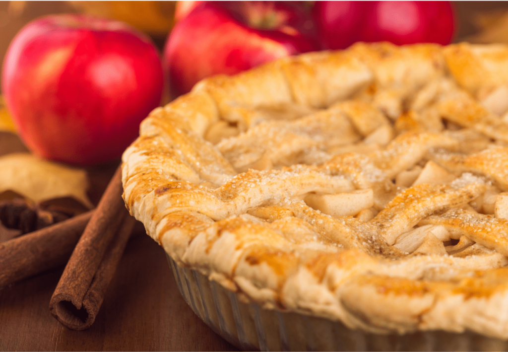Apple pie beside cinnamon sticks and apples